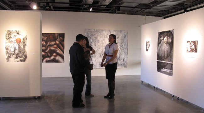 Artist Yvianna Hernandez (right) at UTEP's Glass Gallery surrounded by her drawings and paintings. (Lucía Murguía/Borderzine.com)