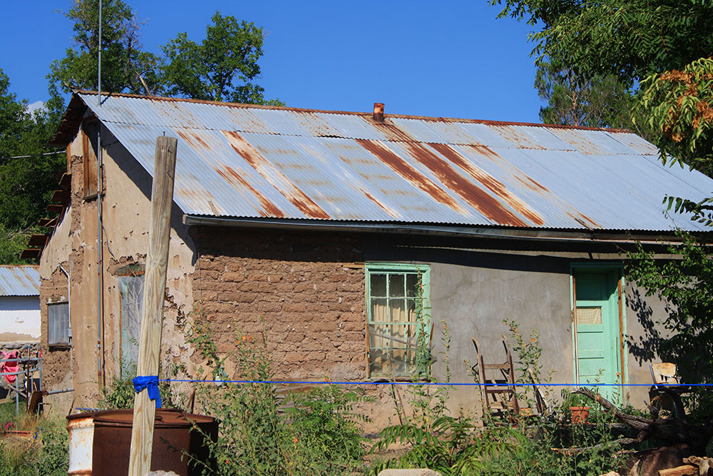 Adobe house, half plastered, half exposed, and rusting tin roof. (Cheryl Howard/Borderzine.com)