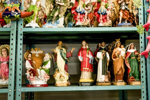 Statues of religious figures line green metal shelves in a shop window.