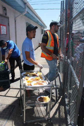 Ali Pérez, a la derecha, junto a Luis Henrique, al centro y Brian Ponzio, derecha, se encargan de repartir la comida cocinada a los inmigrantes.