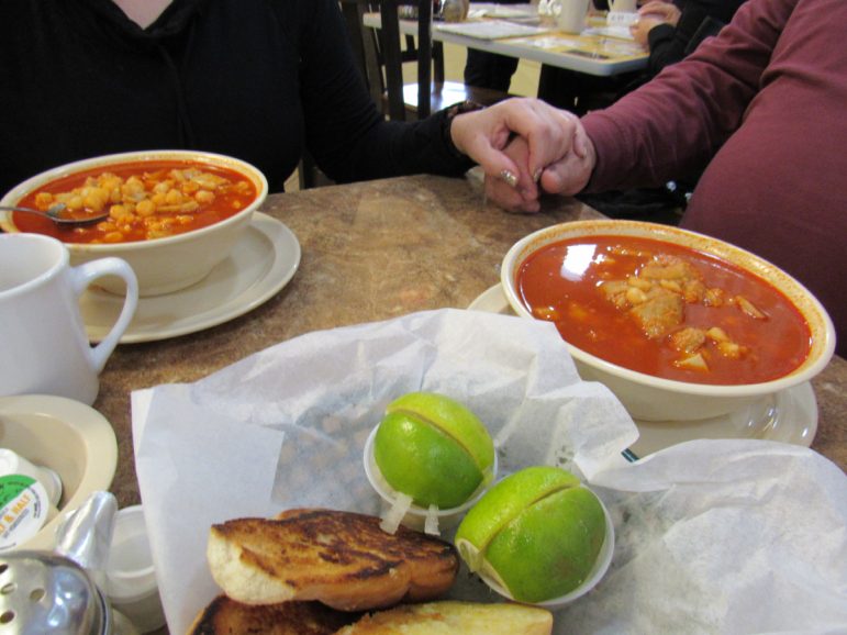 A table is set with pan blanco, lime and two bowls of menudo.